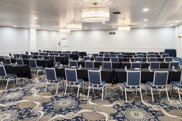 The image shows a conference room with rows of tables and chairs, arranged for a meeting or presentation, featuring chandeliers and patterned carpet.